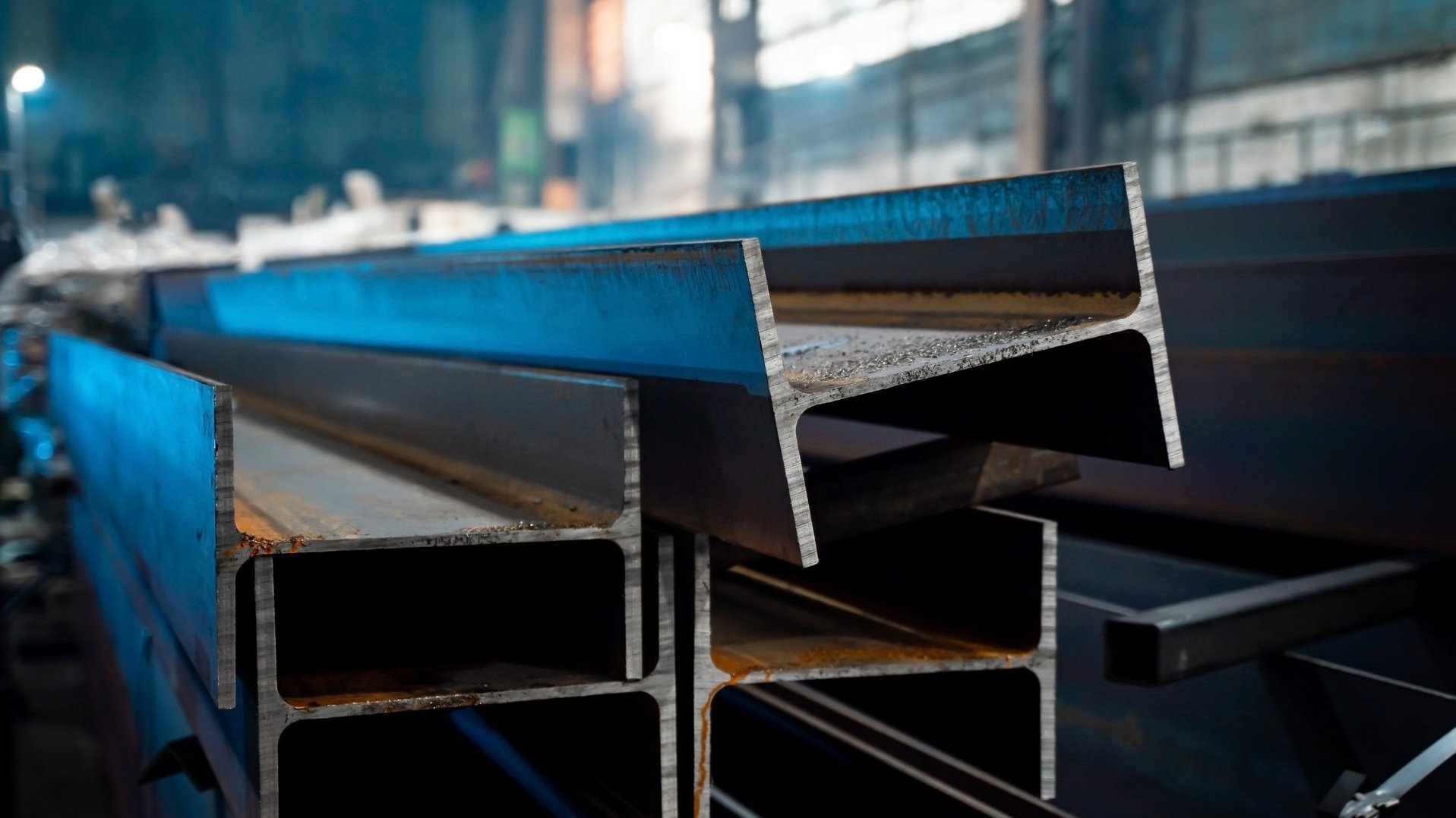 Large metal beams in the production area Stahlträger liegen ordentlich ineinander gestapelt in einer abgedunkelten Fertigungshalle